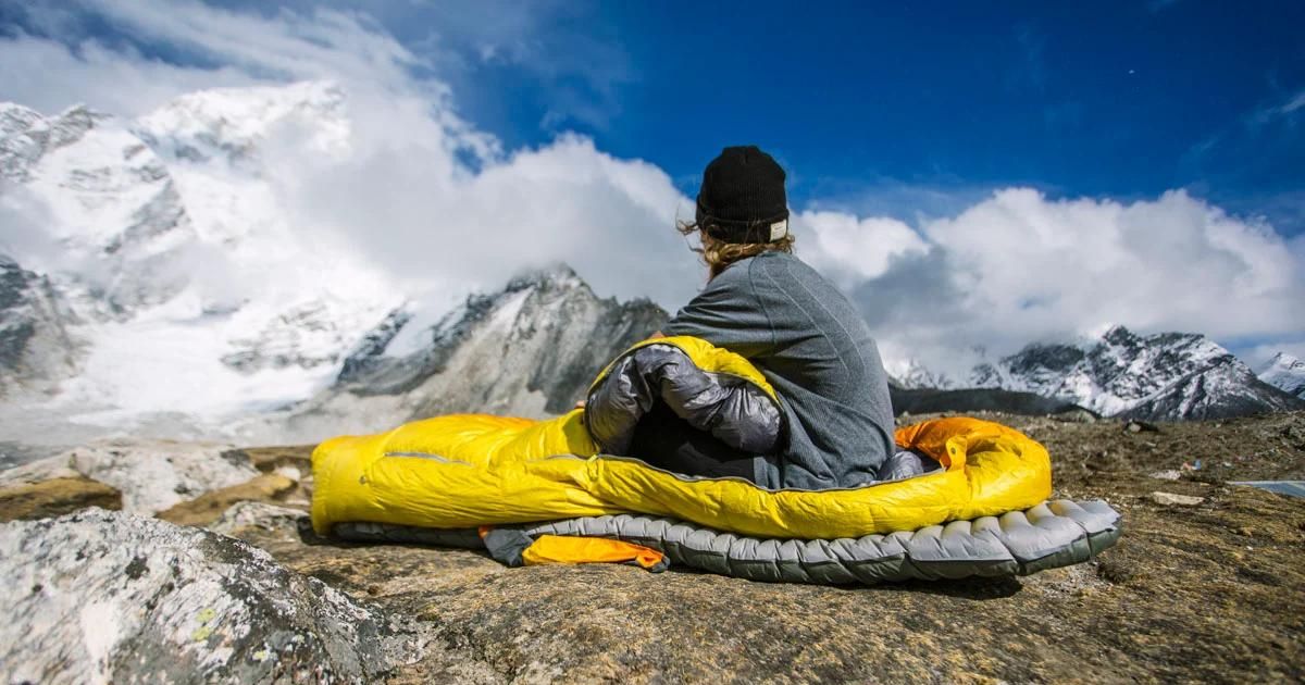 A girl wearing a sleeping bag is looking at a mountain.